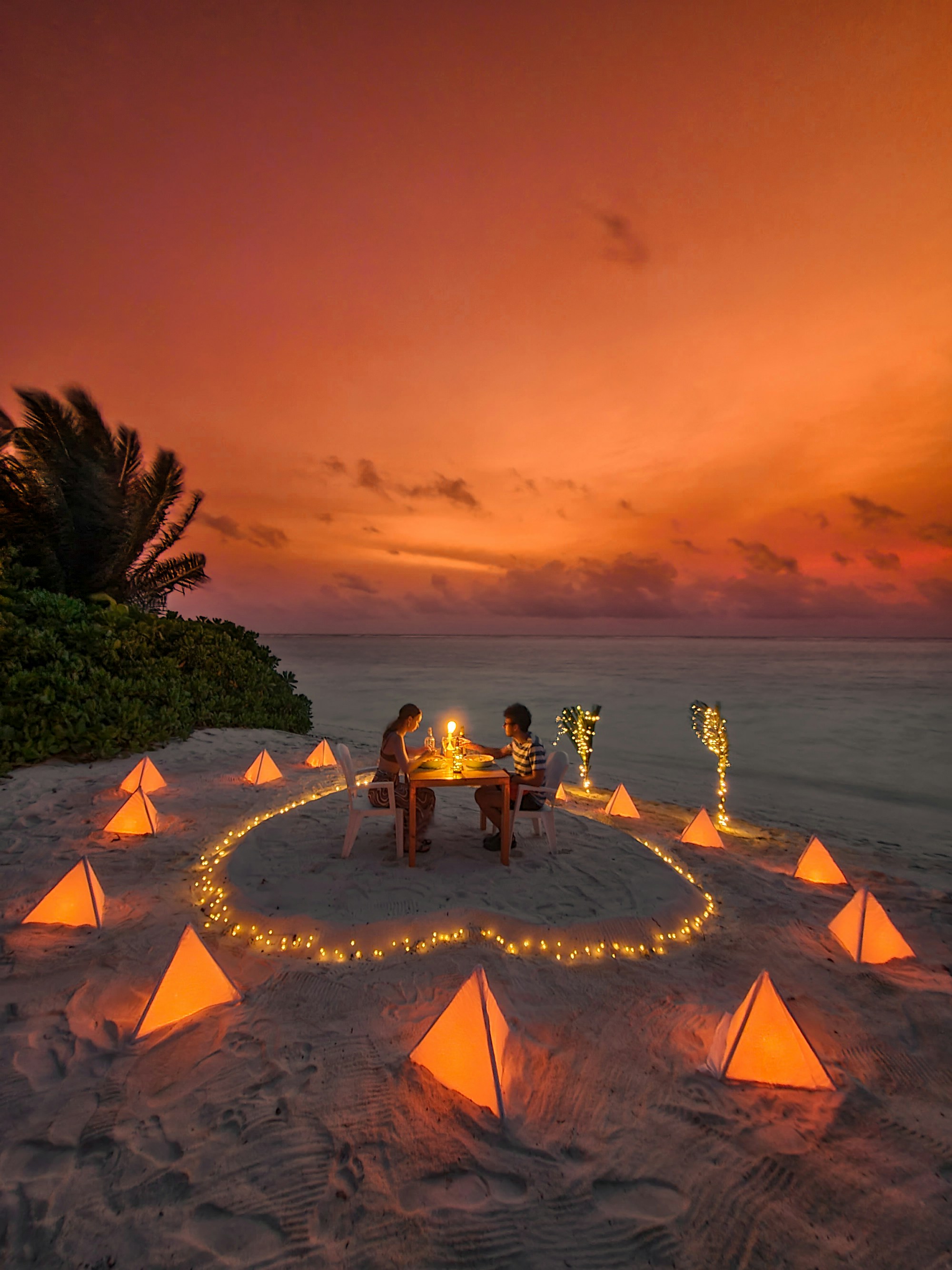 Romantic dinner setup on beach at sunset with lanterns